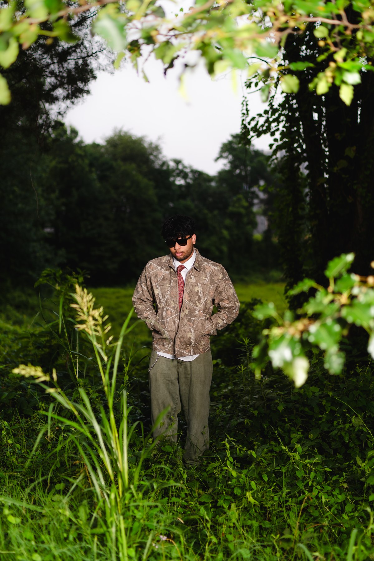 A full-length portrait framed by leafy branches and dense greenery.