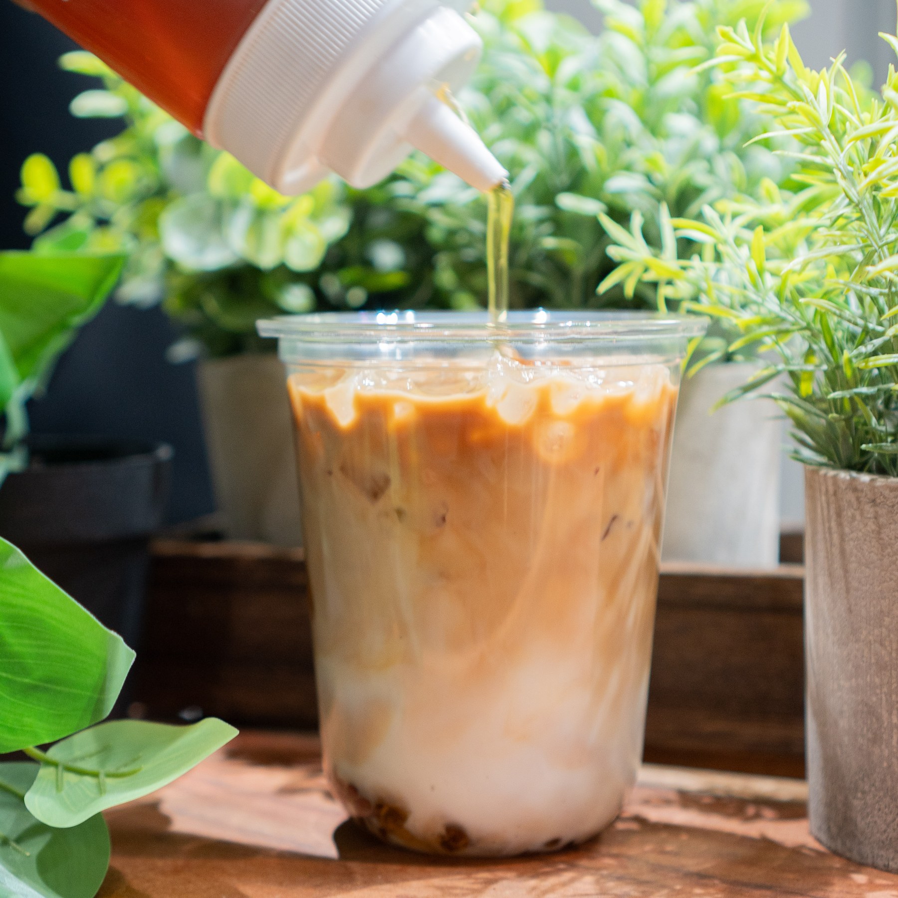 Syrup pouring into an iced latte among green plants at Cafe Hive.