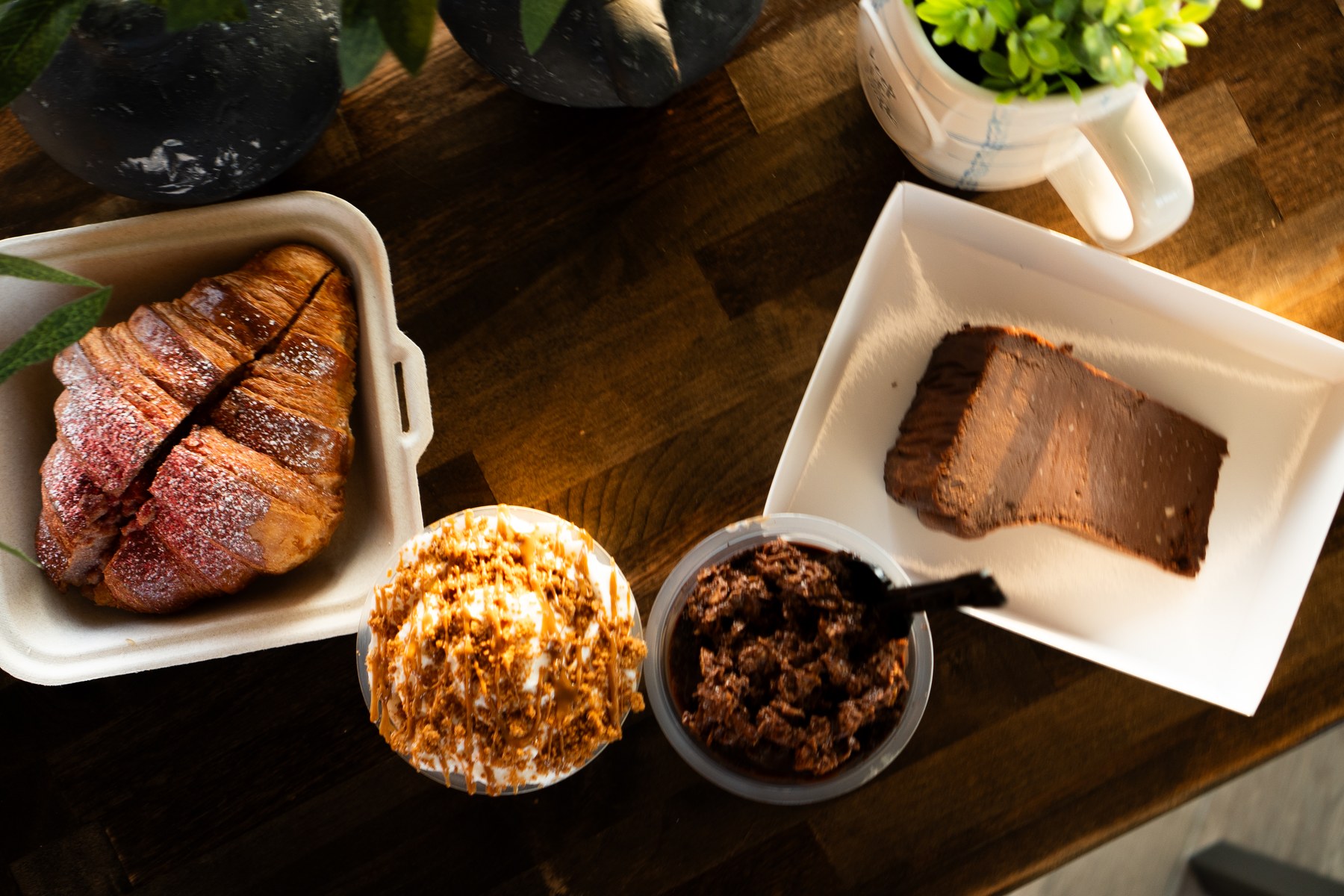 Croissant, cake and layered desserts arranged on a sunlit wooden table at Cafe Hive.
