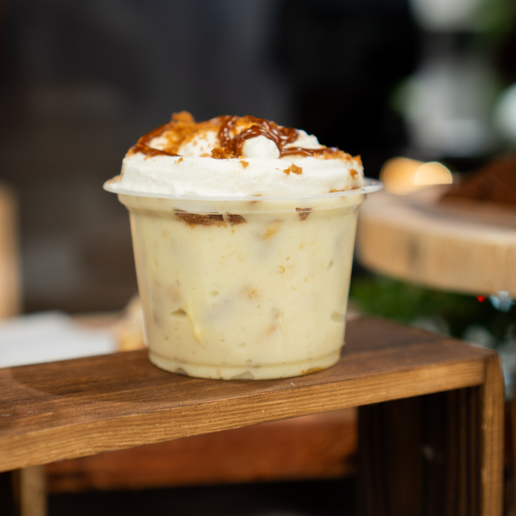 Banana pudding topped with cream and crumbs on a wooden display.