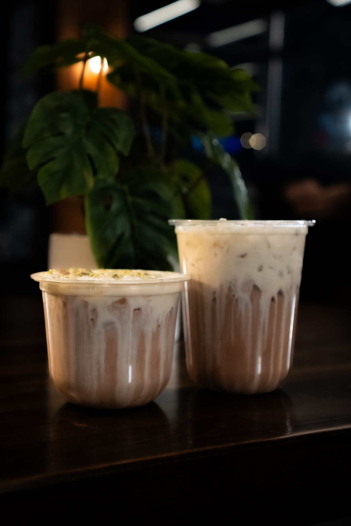 Two pink chai drinks, one short and one tall, on a dark cafe counter.