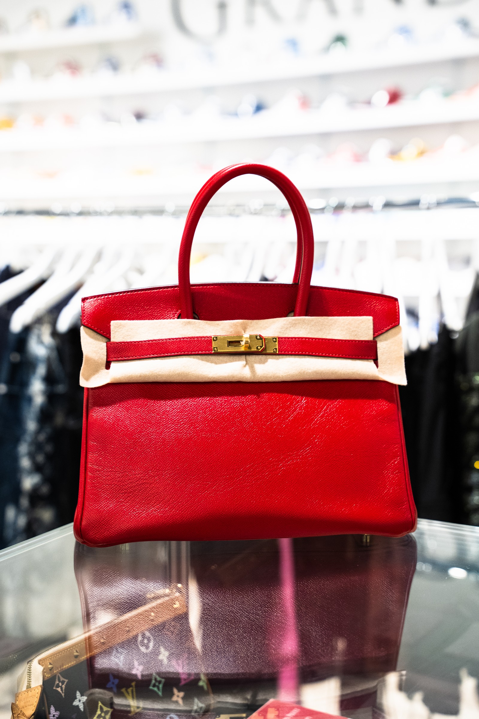 Red structured handbag with gold clasp displayed at Grandeur.