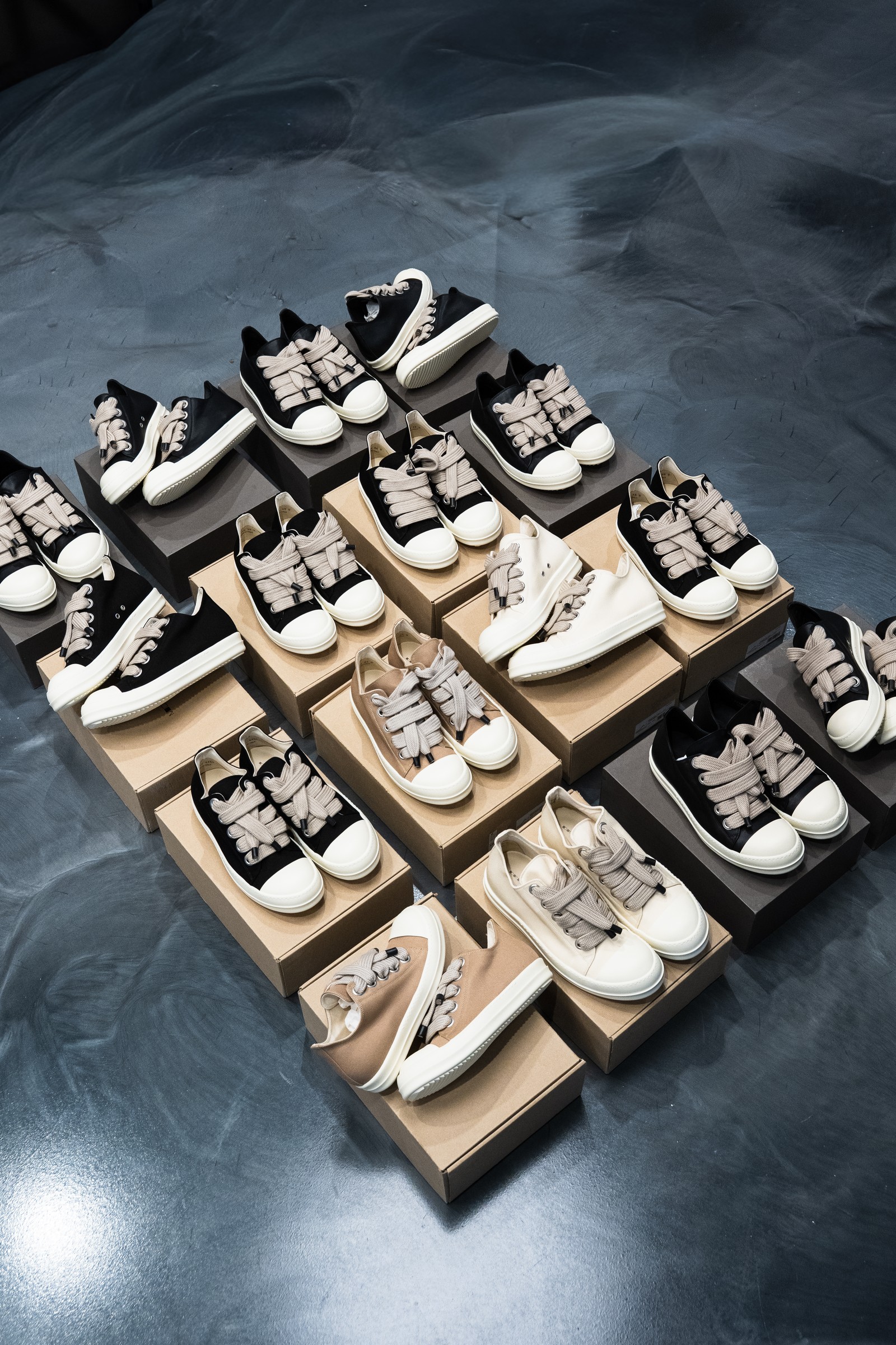 Designer sneaker collection arranged on boxes across a dark floor.
