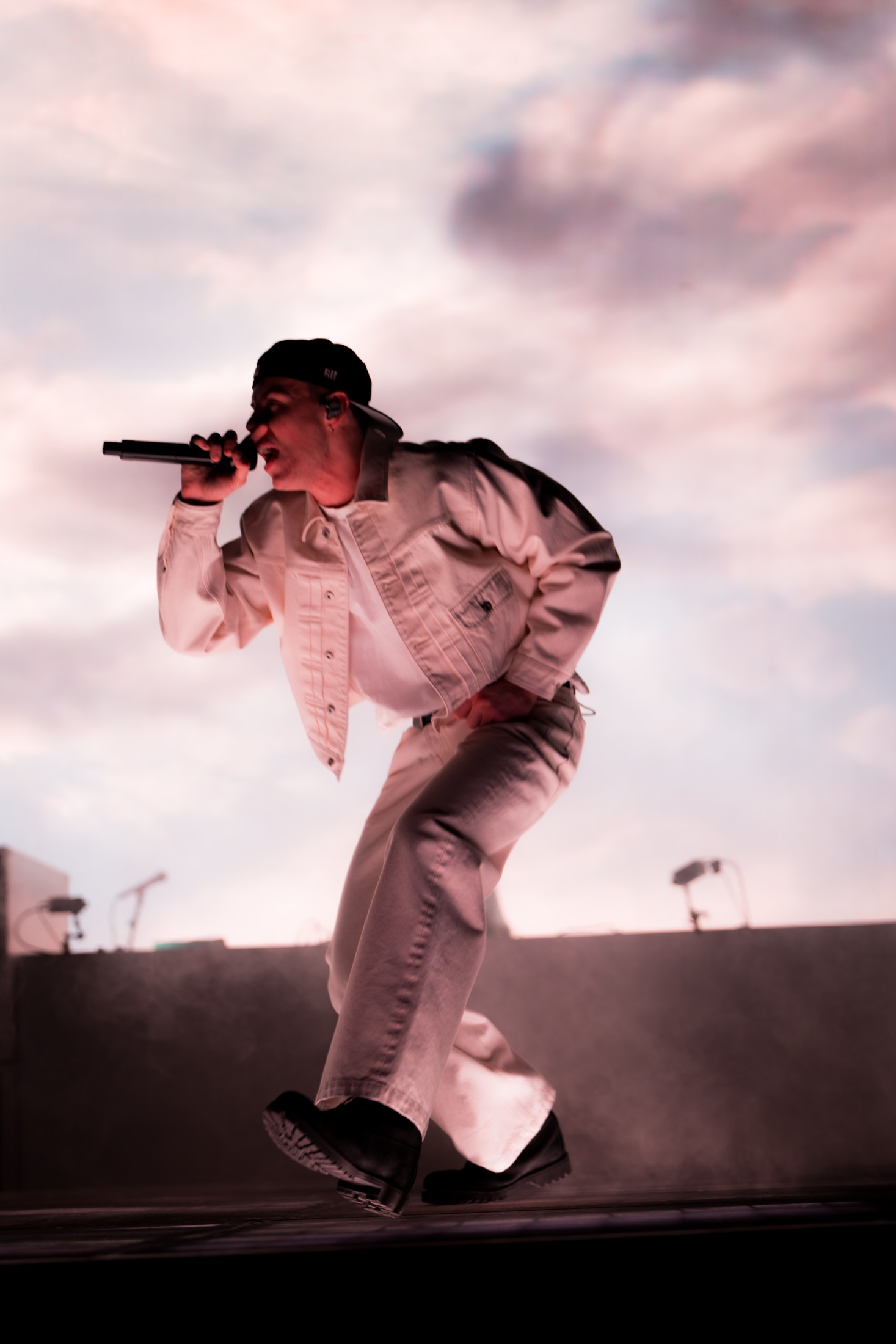 The Kid LAROI leans toward the crowd with a microphone against a pink cloud backdrop.