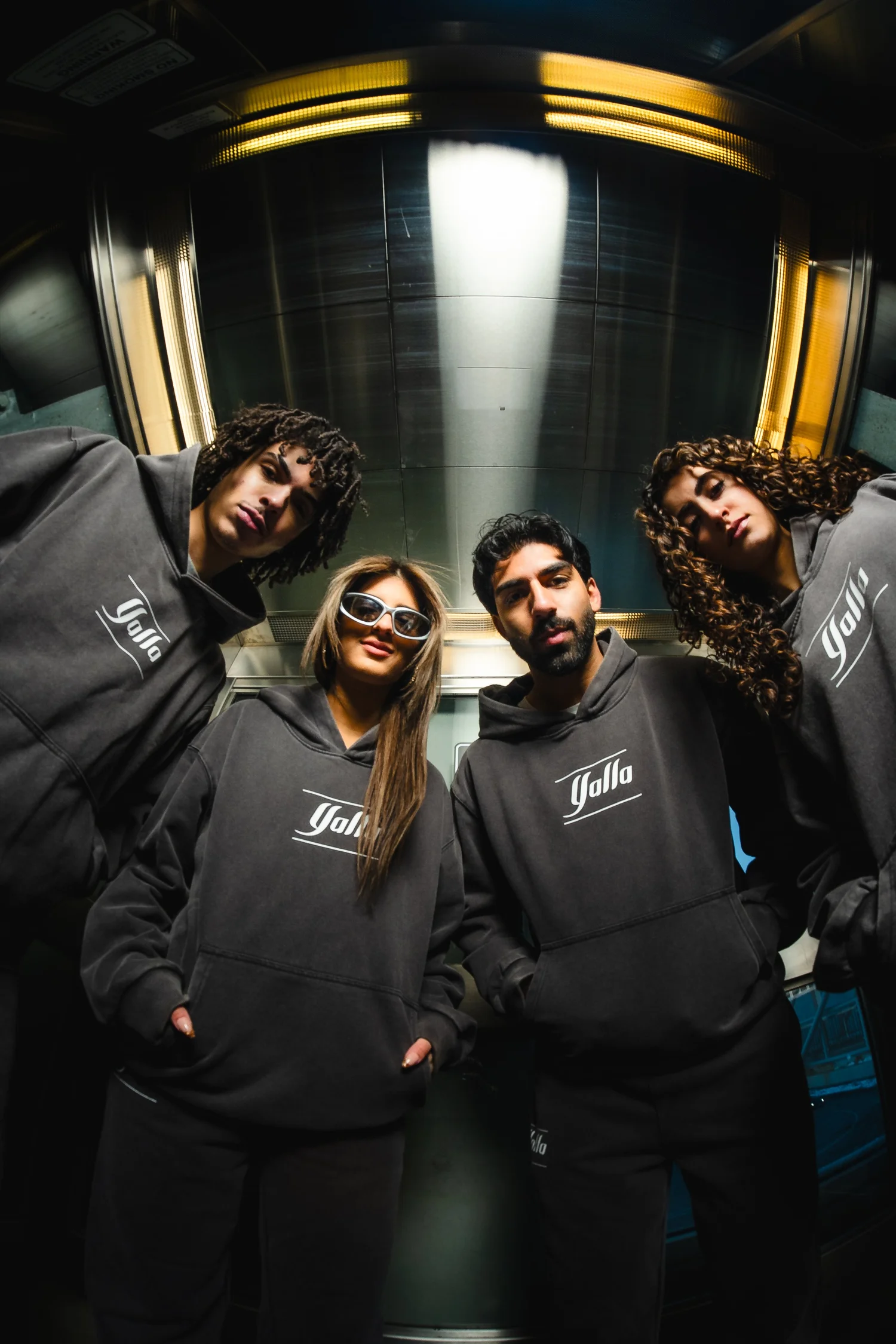 Four models wearing Yalla hoodies in a cinematic low-angle elevator photograph
