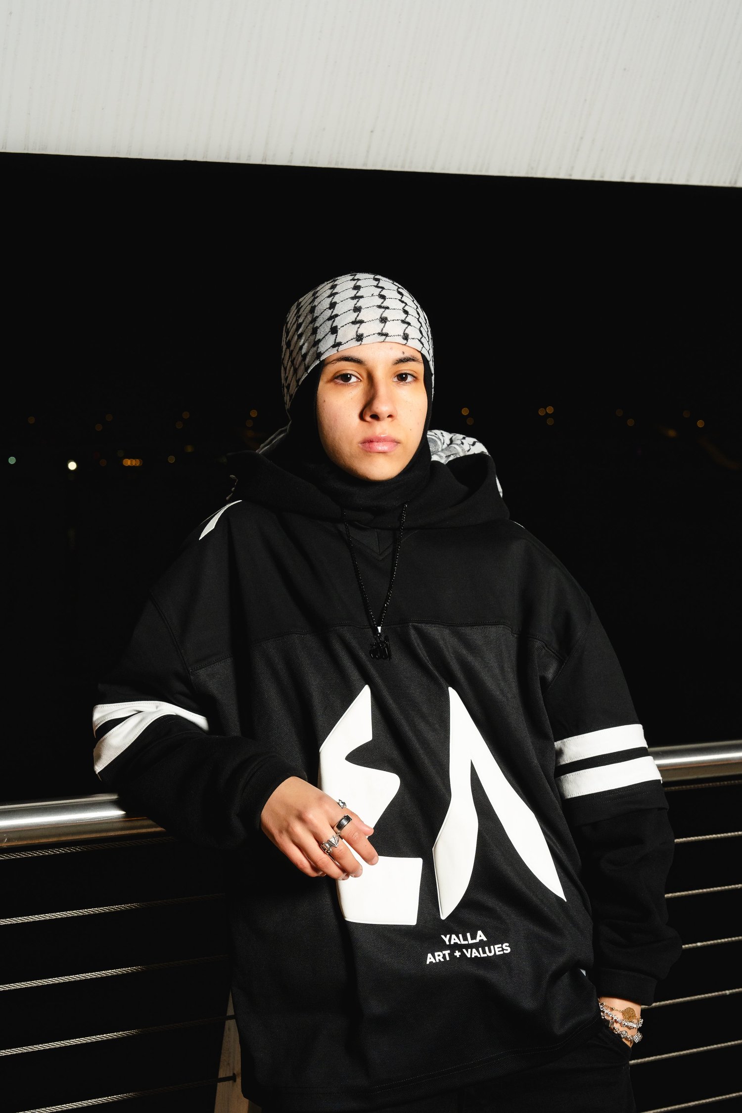 Model wearing a black and white Yalla 48 jersey and head scarf beside a metal railing